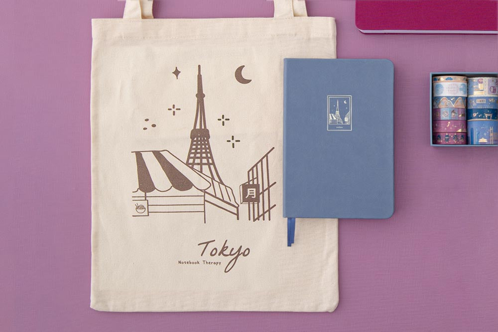 A flatlay of a Tokyo tote bag and a blue notebook with a Tokyo tower design