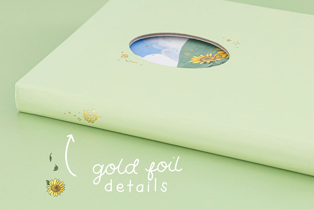 Angled photo of Tsuki Four Seasons Summer Collectors Edition 2022 sage bullet journal notebook showing sunflower gold foil detail on the spine