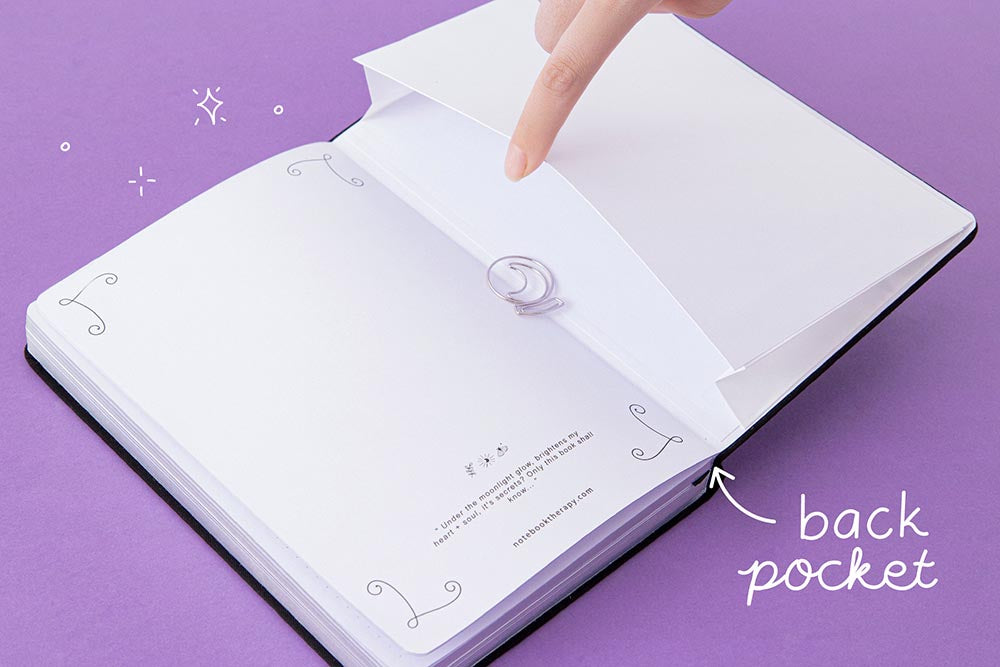 Open back page pocket of Tsuki ‘Moonlit Spell’ Limited Edition Holographic Bullet Journal held in hand with free bookmark gift on purple background