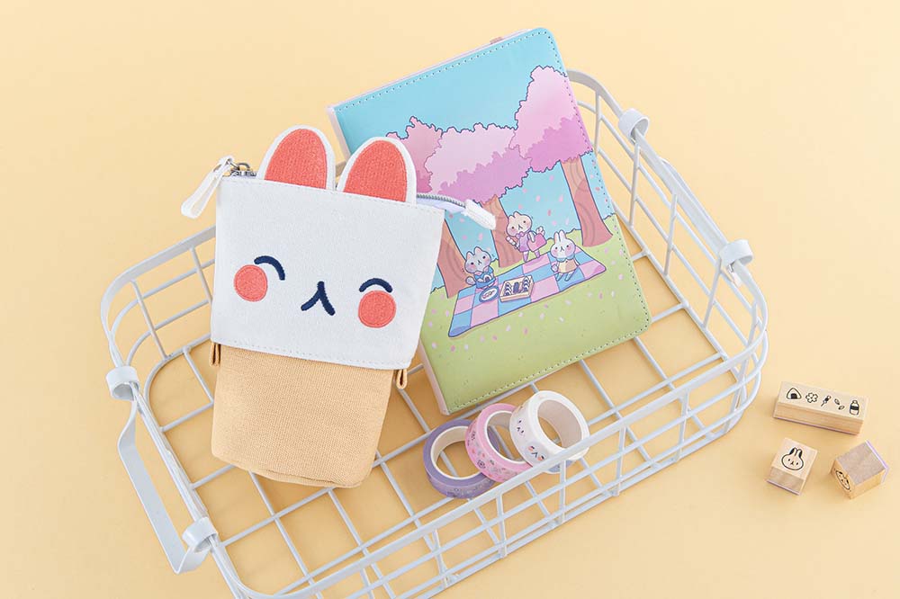 Tsuki ‘Four Seasons’ Embroidered Pop-Up Pencil Case by Notebook Therapy x Milkkoyo in kitty with Tsuki ‘Four Seasons: Spring Edition’ and Tsuki ‘Four Seasons’ Washi Tapes in white basket with Tsuki ‘Four Seasons’ Bullet Journal Stamps on honey yellow background