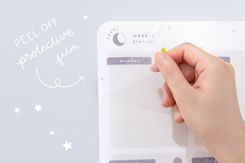 Close up of Tsuki Reusable Wall Planner with peel off protective film held in hand on light grey surface