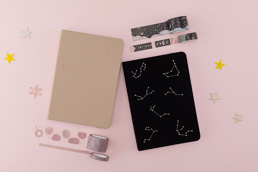 Flatlaay of beige constellation bullet journal and black constellatton bullet journal with constellation themed washi tapes