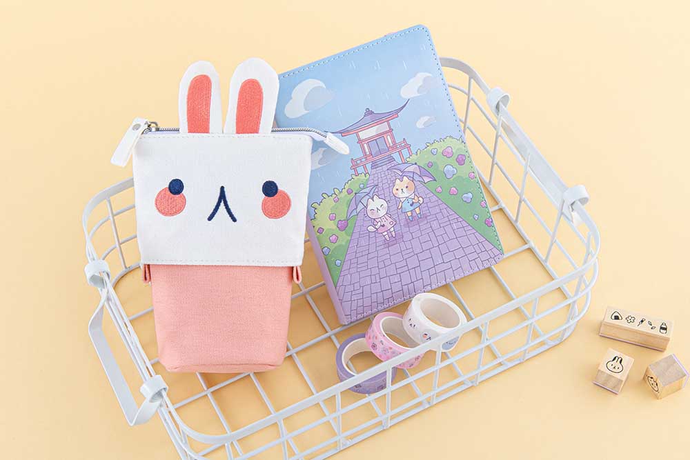 Tsuki ‘Four Seasons’ Embroidered Pop-Up Pencil Case by Notebook Therapy x Milkkoyo in bunny with Tsuki ‘Four Seasons: Summer Edition’ and Tsuki ‘Four Seasons’ Washi Tapes in white basket with Tsuki ‘Four Seasons’ Bullet Journal Stamps on honey yellow background