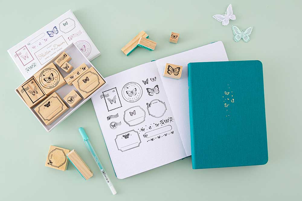 Tsuki ‘Flutter + Dream’ Bullet Journal Stamp Set by Notebook Therapy x Pelinkan with two Tsuki Teal Sky ‘Flutter + Dream’ Limited Edition Bullet Journals by Notebook Therapy x Pelinkan with gelly pen and butterflies on mint background