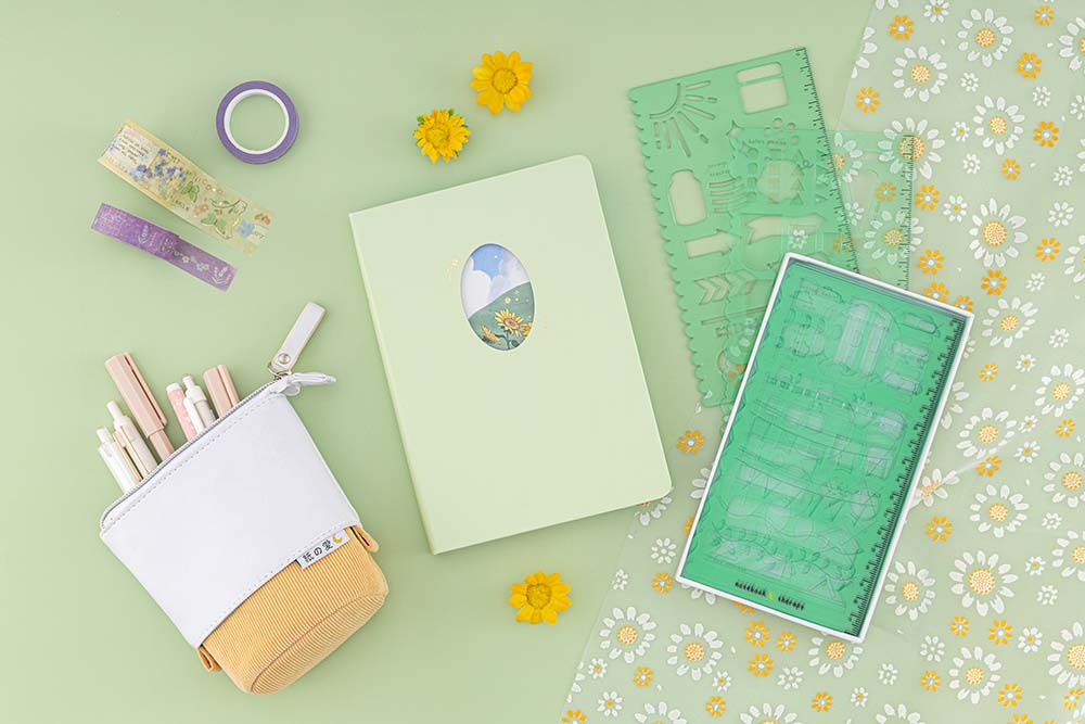 Flatlay photo of Tsuki Four Seasons Summer Collectors Edition 2022 sage bullet journal notebook with honey butter yellow pop-up pencil case and green Tsuki bullet journal stencils on sage green background