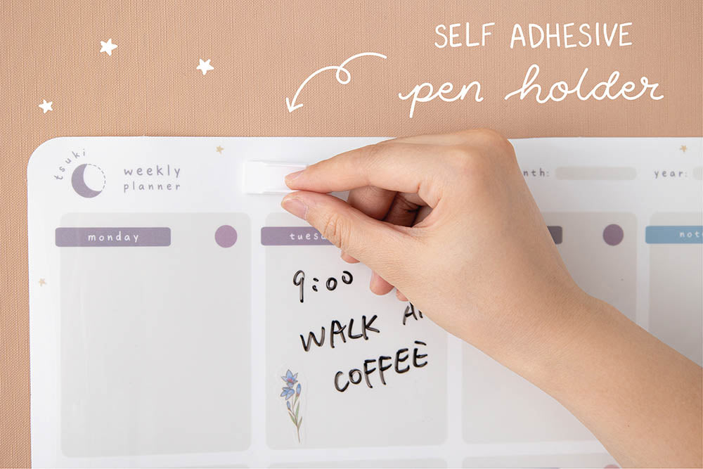 Close up of Tsuki Reusable Wall Planner with free self-adhesive pen holder held in hand on smooth wallpaper surface