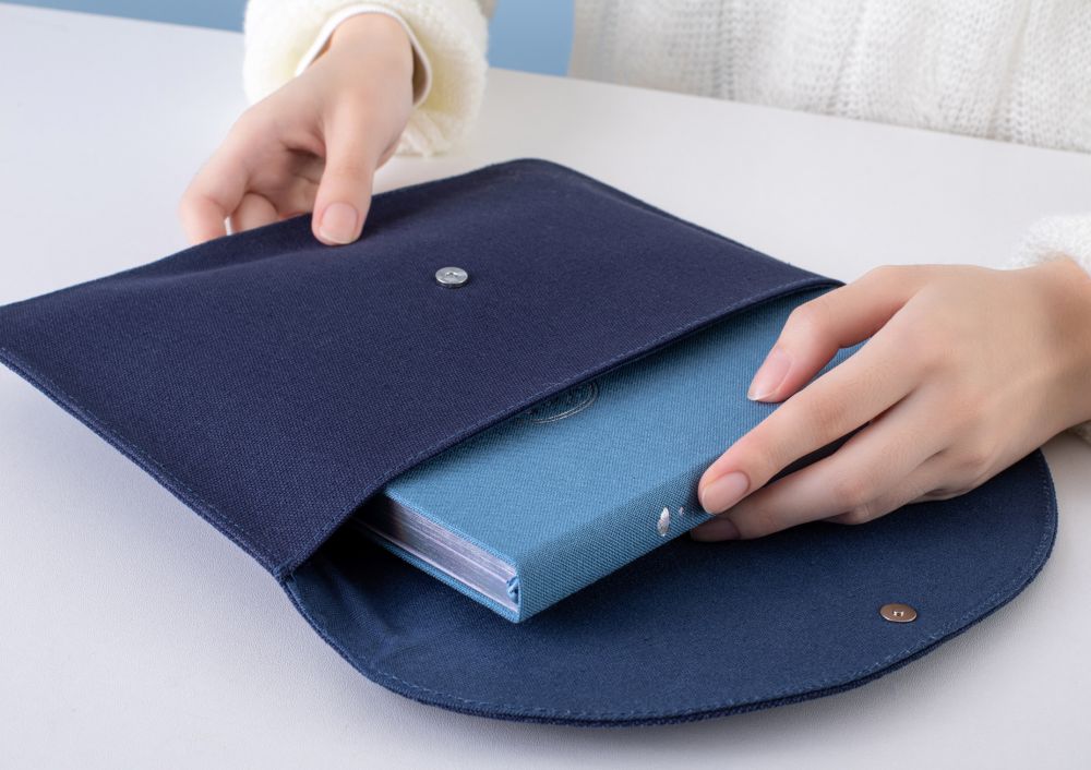 Hands putting a notebook inside the Cloud Dreamland notebook pouch on a white table