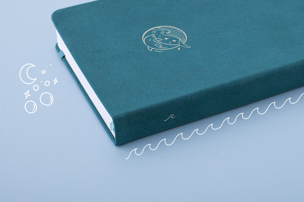 Close up of the spine of Sea green textured leather Tsuki Dolphin Days bullet journal on blue background