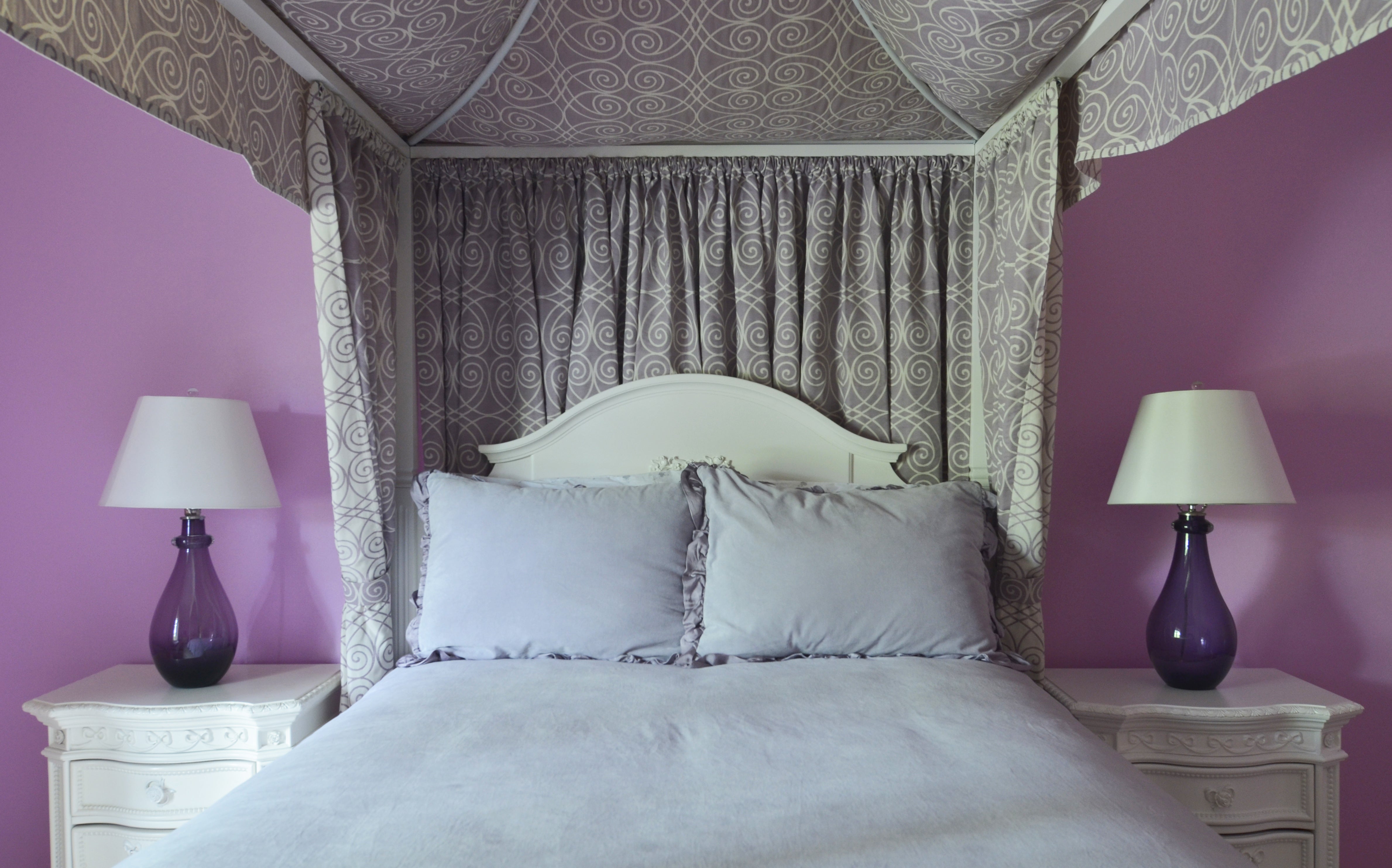 White canopy bed adorned in lavendar with purple lamps flanking