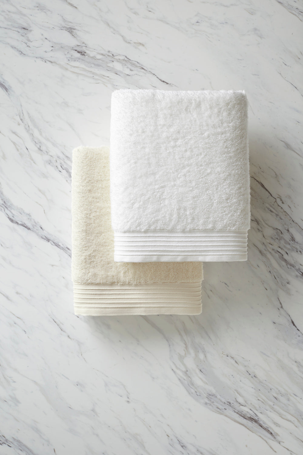 Minimalist folded Bamboo towels in white and ivory on a white marble background