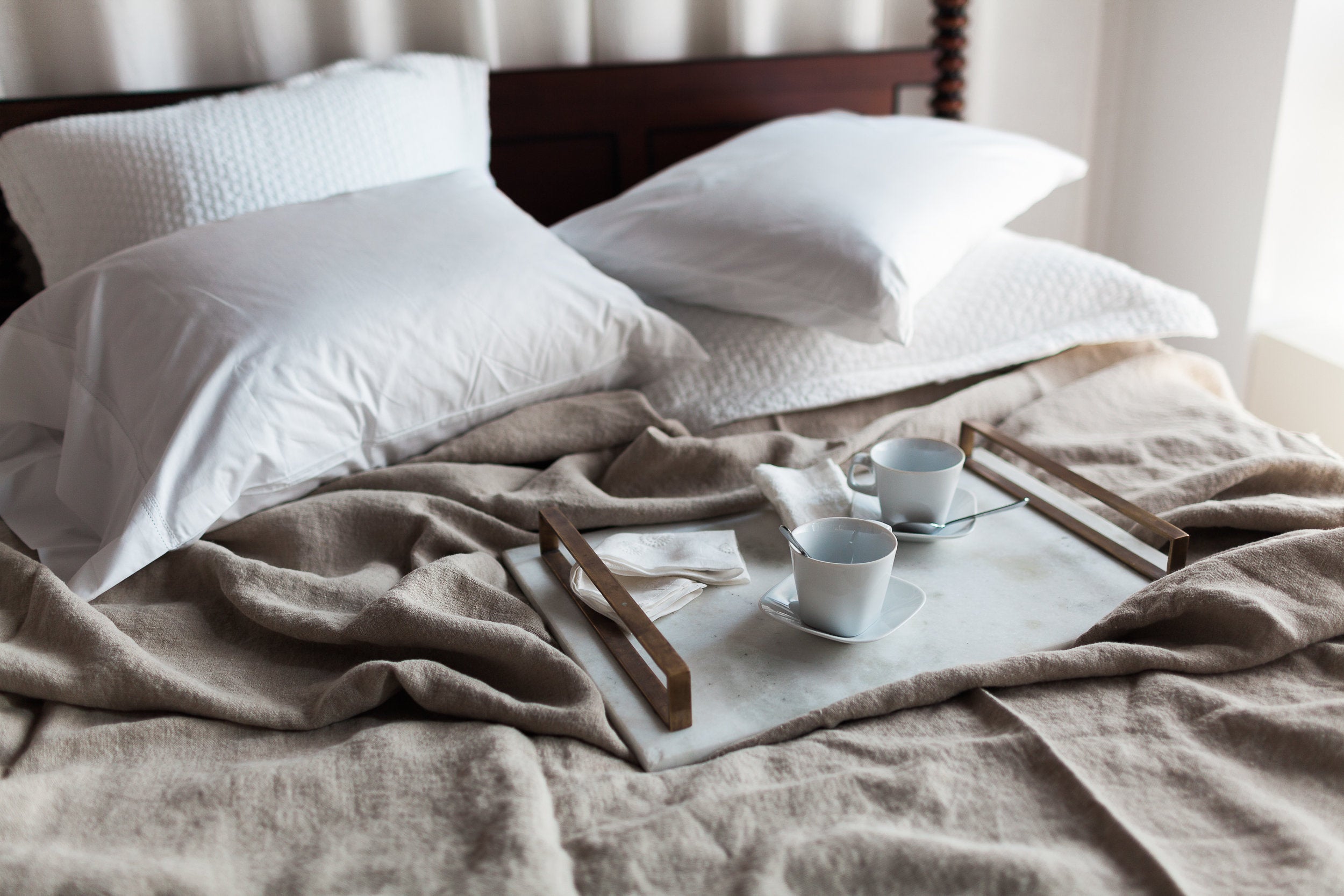 Messy bed featuring various textured linens with a breakfast tray and empty coffee cups