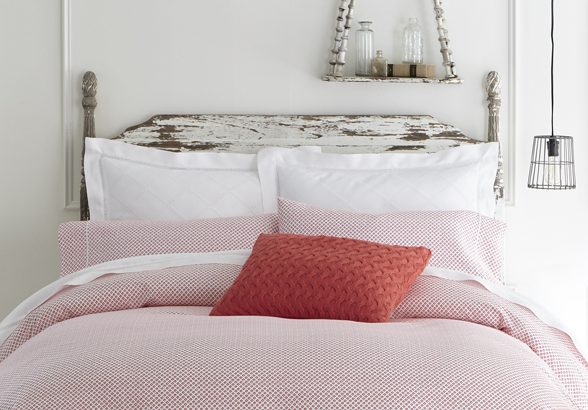 Country style bed made up in red and white with a cable knit throw pillow on top