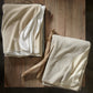 Folded Alta Reversible Cotton Blanket On Table White Pearl Colors