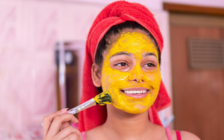 Beautiful girl applying turmeric yellow face mask on face through brush