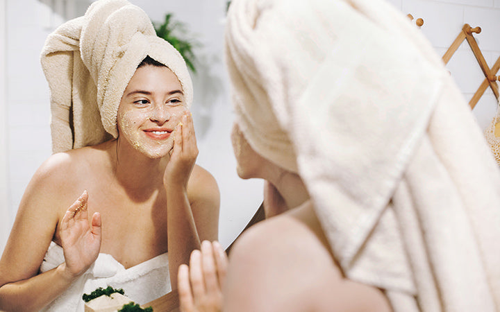 Happy woman in towel making facial massage with organic face scrub