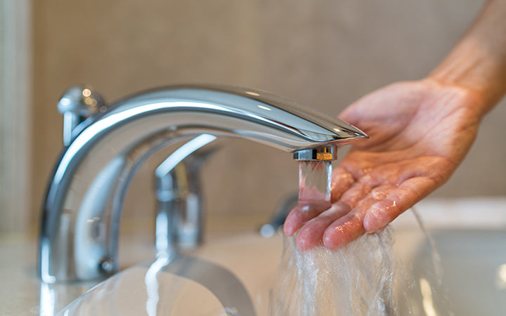 Woman checking temperature touching running water with hand