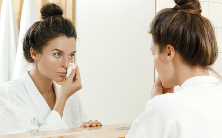 Woman is looking in to the mirror and removing makeup