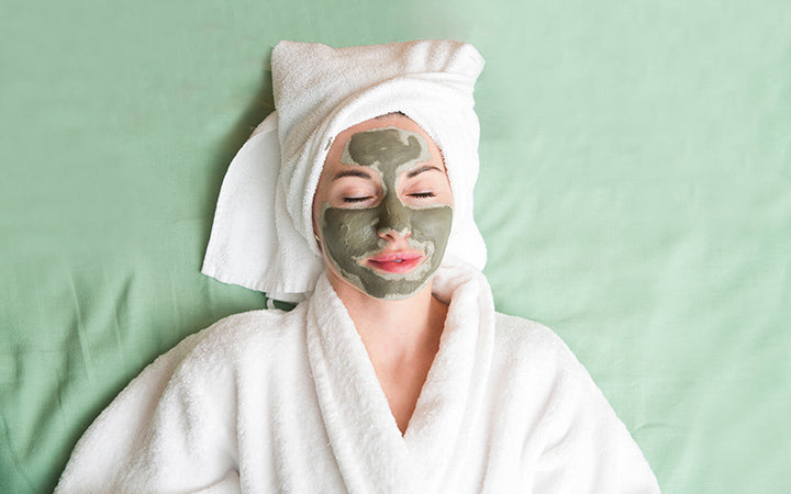 Woman wearing bathrobe and towel on her head applying facial mask