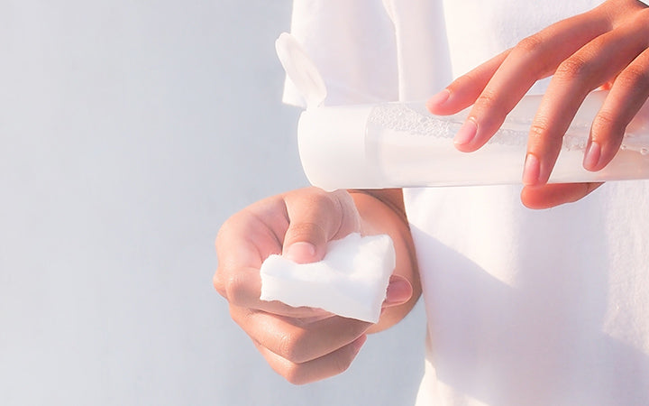 Woman with cleansing toner bottle and cotton to clear skin.