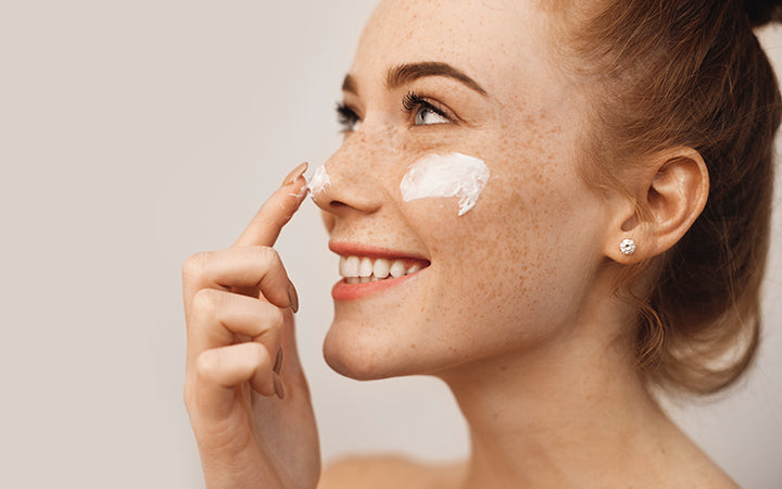 Young woman applying cream on her face and nose with finger