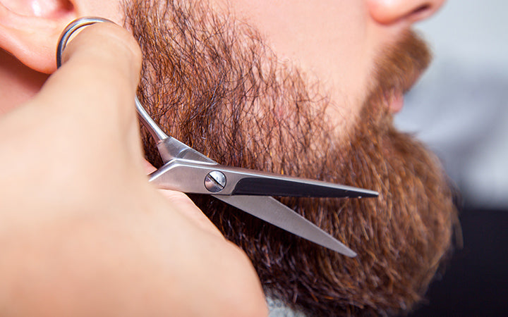 barber with scissors shaving bearded man