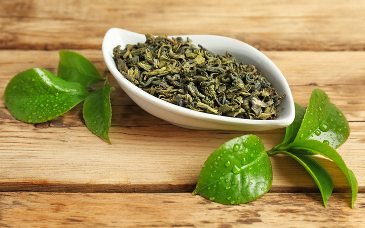 bowl with dry tea and green leaves on wooden table