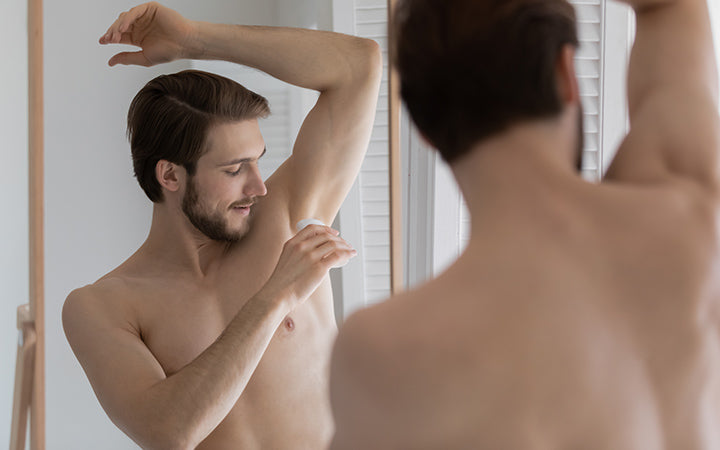 mirror reflection young man applying antiperspirant on armpit after shower
