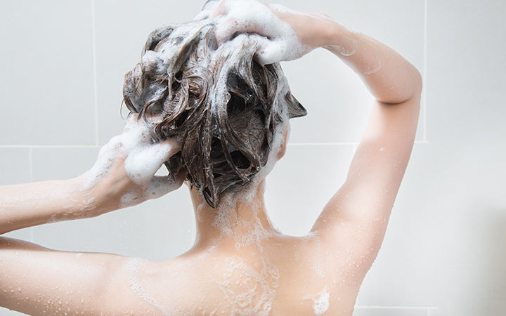 woman in shower washing hair with shampoo