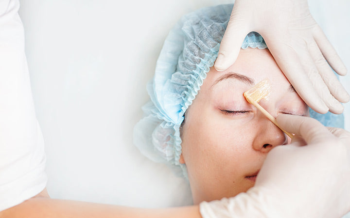 woman in spa salon receiving epilation or correction eyebrow using sugar