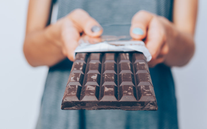 woman's hands holding unwrapped dark chocolate bar