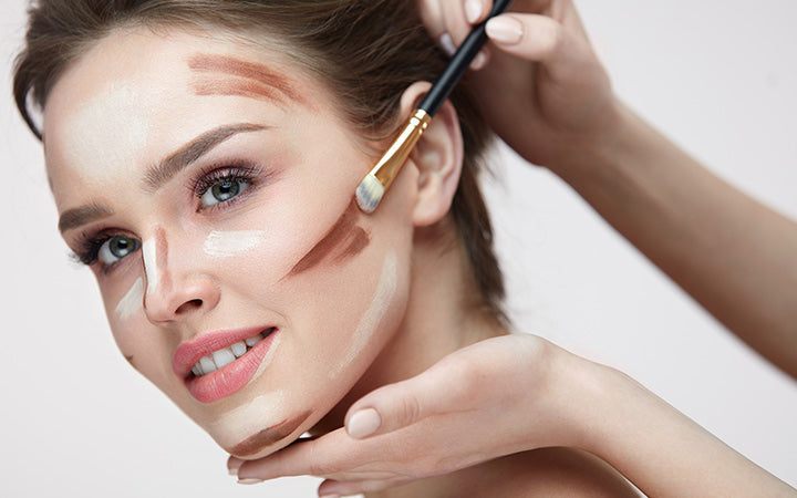 young female with smooth skin and fresh makeup and hands with brush applying make-up product