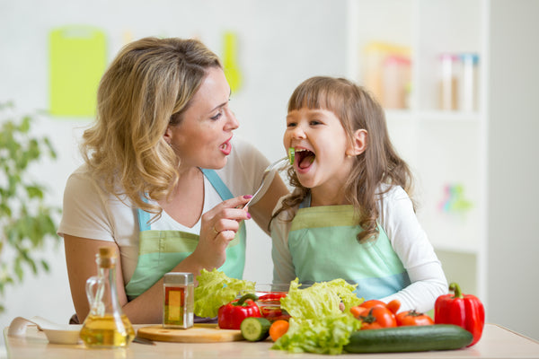 A mother feeding her kid vegetables. 