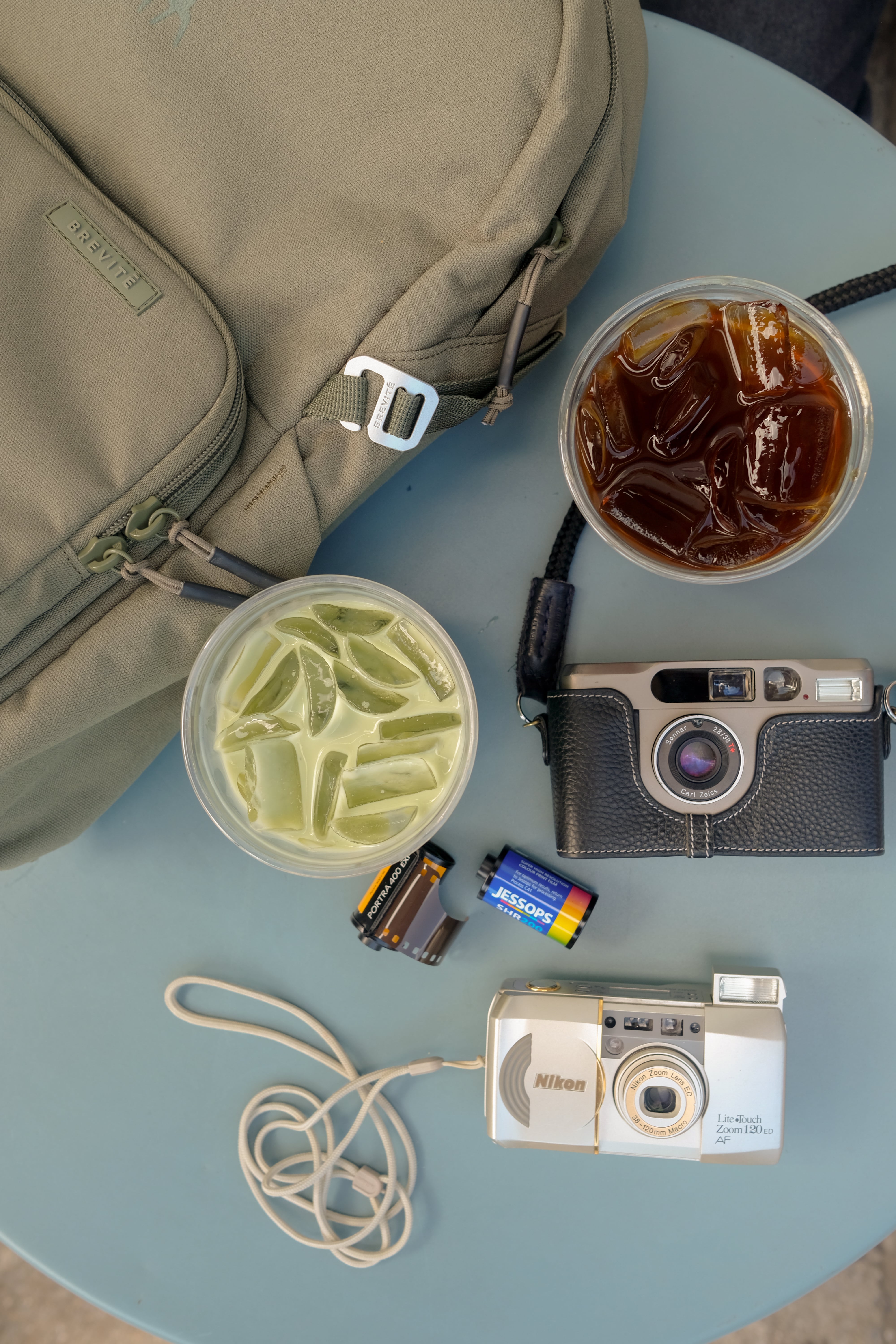 Aerial view of drinks, cameras, and a backpack on a table.