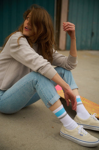 Skateboarder Sierra Prescott sitting on concrete wearing jeans and her signature SOCCO socks.