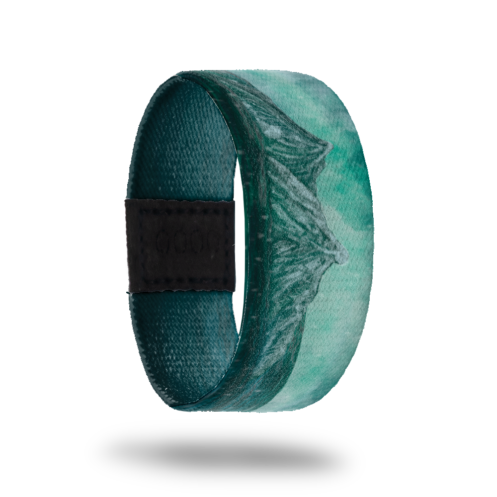 This is a reversible strap. The design is various colors of teal with the scene of mountains in the distance.  The inside is all teal gradient and says Beneath the Surface. It is reversible. 