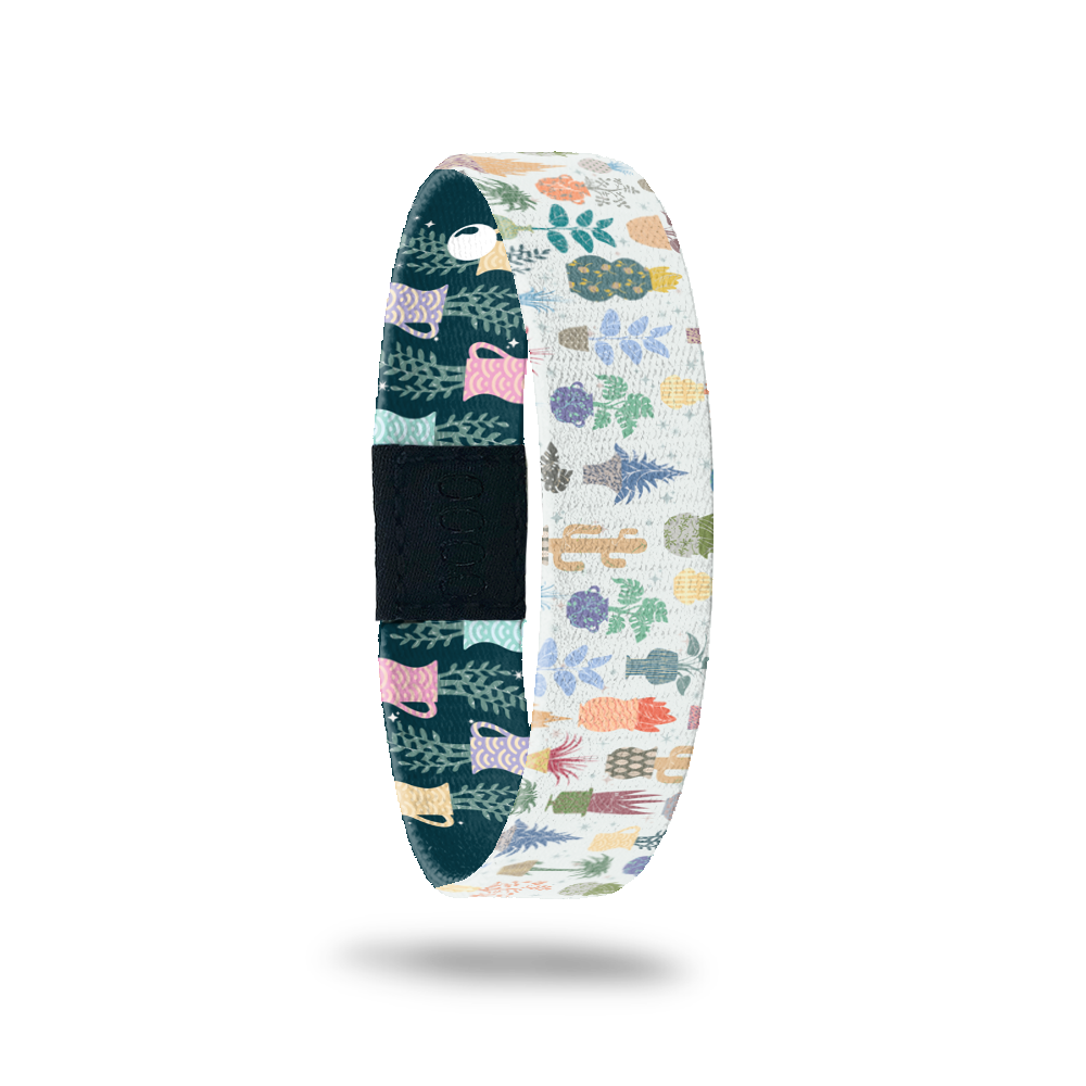 Wristband single with white base and plants/cactus all over in multiple colors. Inside is the same except with a navy blue base and says Grow With It. Comes with a matching pin and collector's box.
