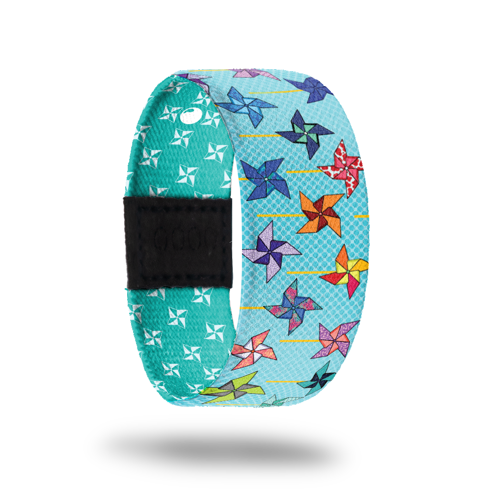 Wristband strap is light blue with pinwheels of diffretn colors all over. The inside is darker teal with white pinwheels and says Its Your Turn. Comes with a matching pin and collector's box. 