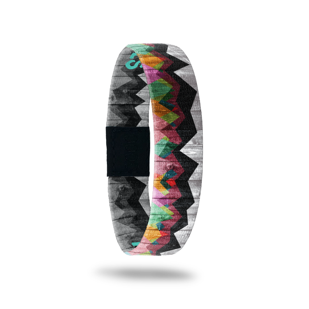Single wristband with two design in one. The background design is a black and grey weathered picket fence and has a grainy look to it. Over top about 3/4 showing, is abstract mountains of varying colors. The inside is the same design and reads Mountains to Molehills. 