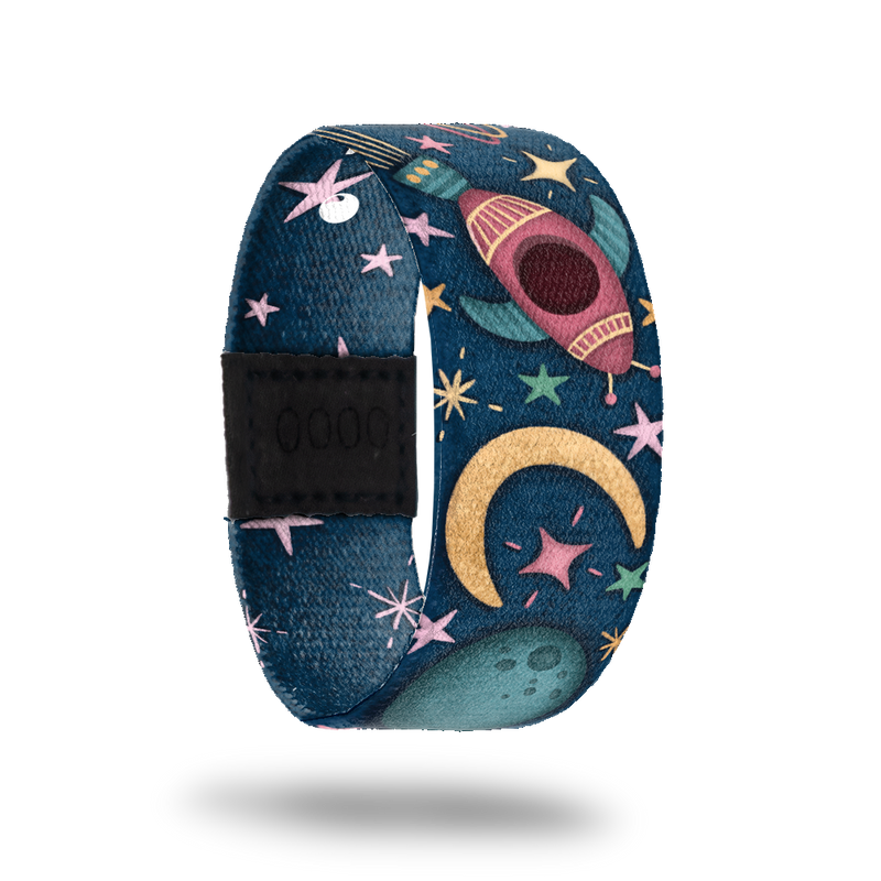 Wristband strap with a dark blue base of space. It has pastel colored stars and bursts with cartoon space ships flying through space. The inside is bluw with all light pink stars and reads One In A Lifetime. This comes with a matching lapel pin and a collector's box. 