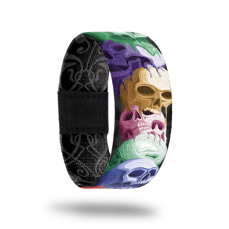 product image of front of wristband named Reflect. The design is a stack of hand drawn skulls in different colors such as purple, gold, pink, blue, and green