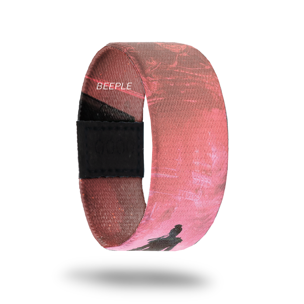 outside product photo of a wristband named Show Up designed by Beeple. It is mainly pink and red and features a darker silhouette of a warrior walking down a road to a larger lighter colored warrior that appears to be in the sky 