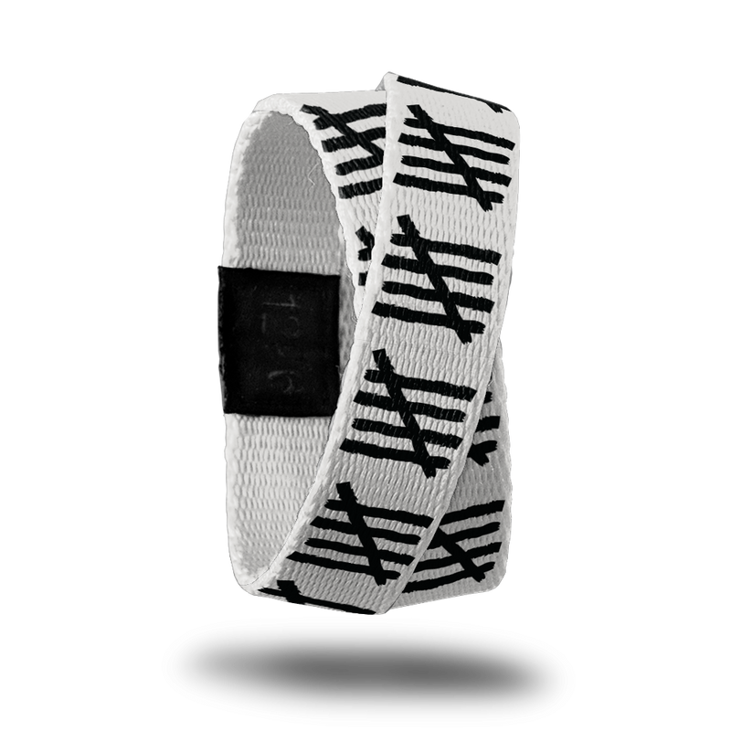 Outside design of Count You Blessings is a white-grey background with a repeated patten of the image of four black lines with one black line running diagonally across the four black lines. This product, called a double, is thinner and wraps around your wrist twice with the material crossing at one point.