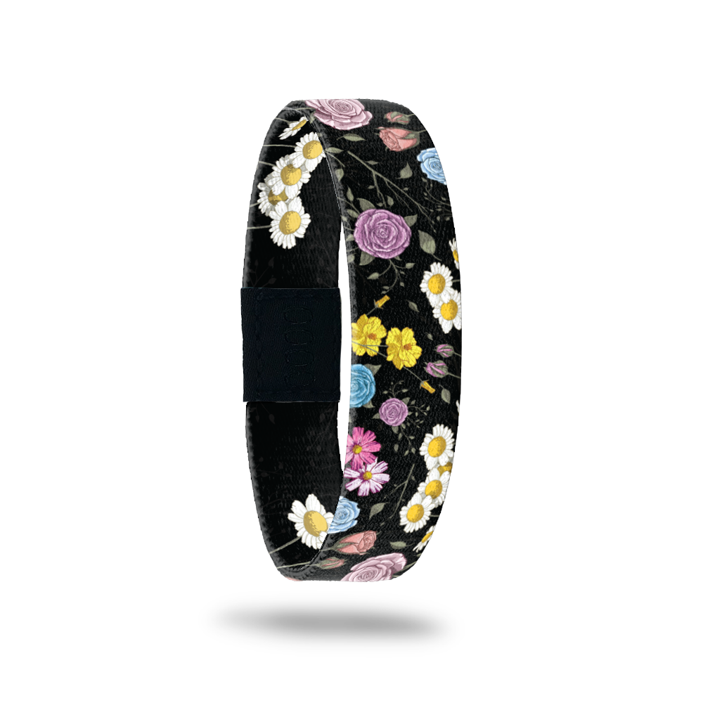 Wristband single that has a black base. The design is all different kinds and colorss of flowers. The inside is the same and says In A Field Of Roses...
