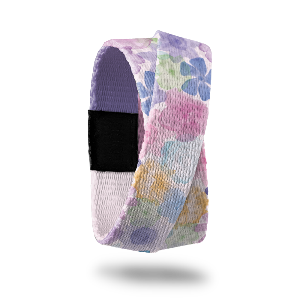 Wristband single that wraps around your wrist 2x. The design is a pastel watercolor of purple, pink, green, blue and orange flowers all over. The inside is a gradient purple solid color and reads Let Go and Let God.