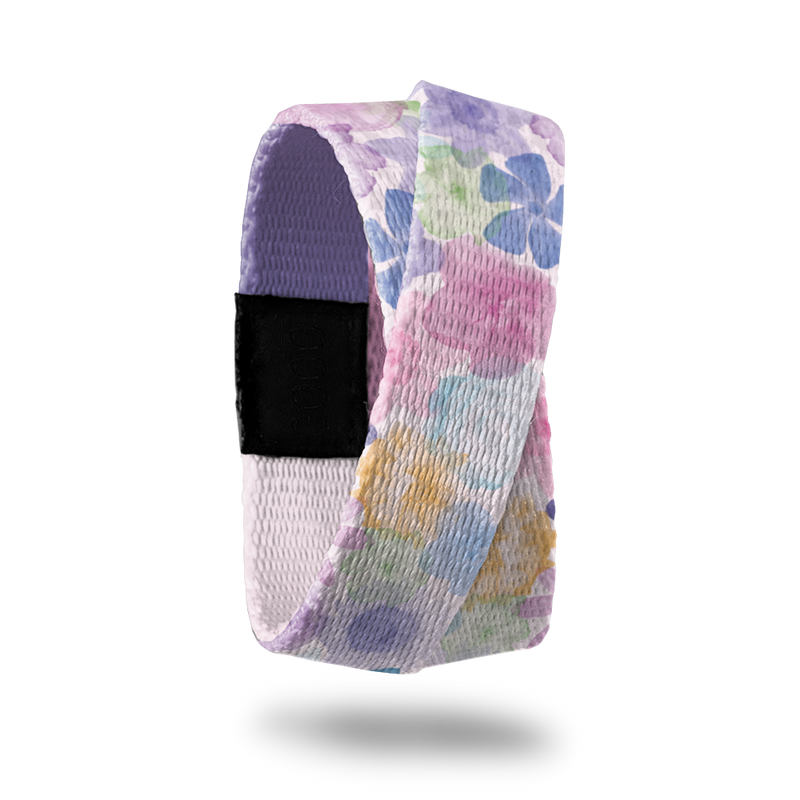Wristband single that wraps around your wrist 2x. The design is a pastel watercolor of purple, pink, green, blue and orange flowers all over. The inside is a gradient purple solid color and reads Let Go and Let God.