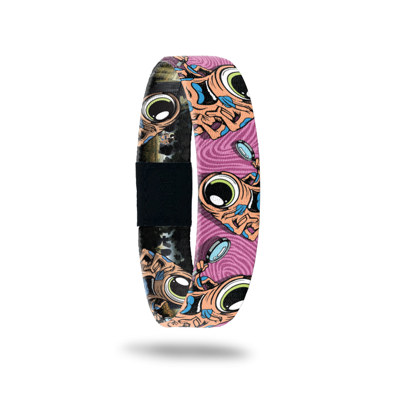 Pink swirly background with the monster in orange.  Monster is on the ZOX multiple times, has 1 eye, a blue tongue and a magnifying glass. Comes with a matching monster pin.