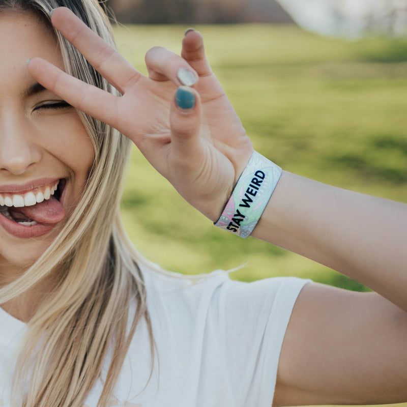 Lifestyle image of someone sticking their young out and giving the hand peace sign with Stay Weird on wrist