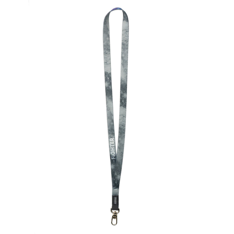 A product image of a ZOX lanyard showing the back of the design with a gold colored metal clip. The lanyard is called Fighter and the design is a greyscale version of the front design which is a space nebula image