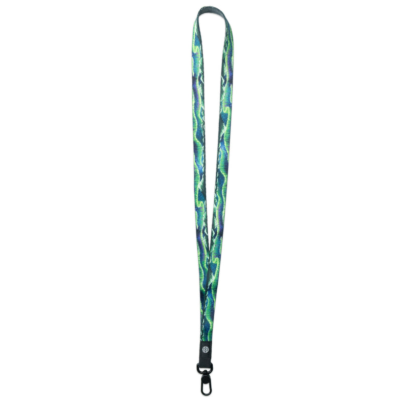 A product image of a ZOX lanyard showing the front of the design with a black colored metal clip. The lanyard is called Live In the Moment and the design is a a blue and green painting of the northern lights 