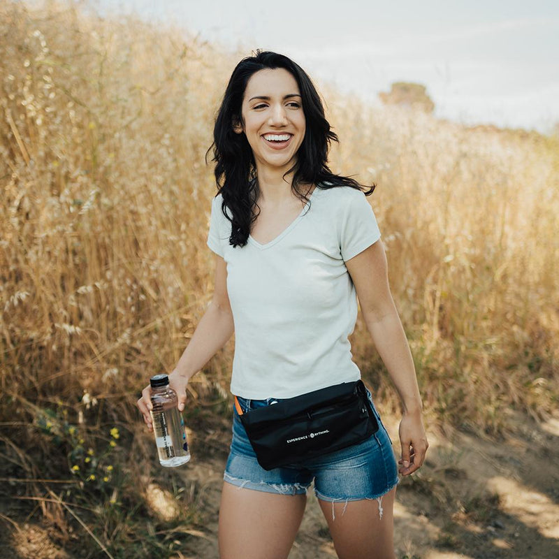 life style photo of a woman on a hike with the fanny pack around her waist with a water bottle in her hands